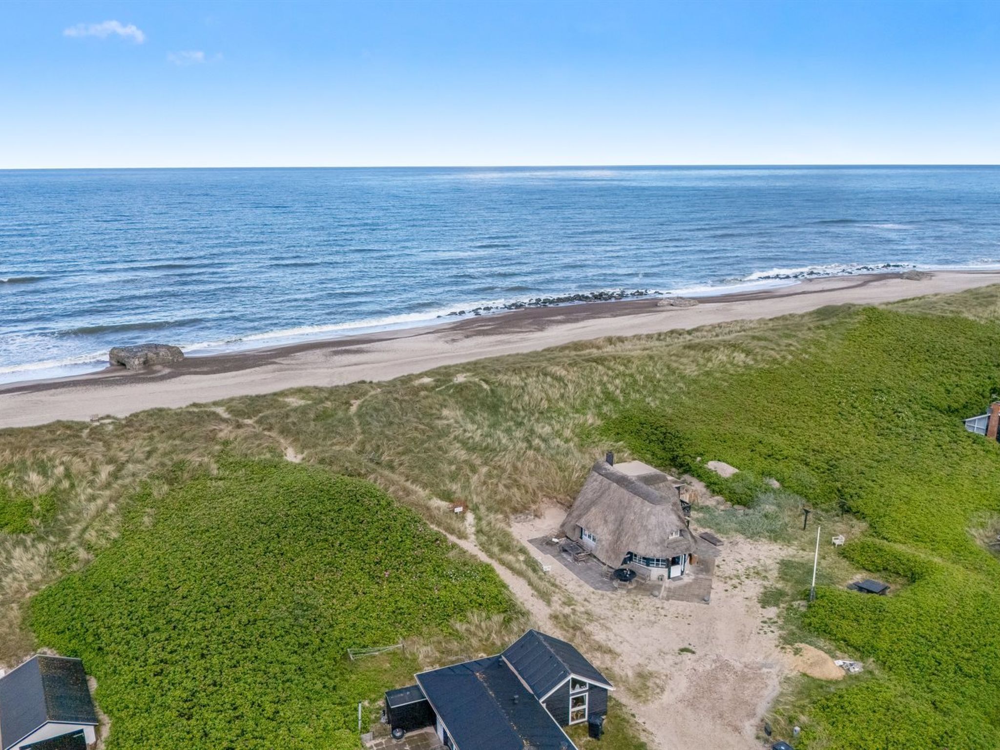 A coastal landscape with a beach, grassy areas, and a thatched-roof building.