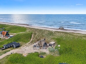 A coastal property with multiple buildings, including a large house with a distinctive roof, situated on a grassy hill overlooking the sea.