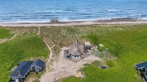 Una propiedad costera con una casa de techo de paja, una playa de arena y una zona ajardinada.
