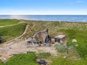 A house with a unique thatched roof, situated on a dune with a view of the sea.