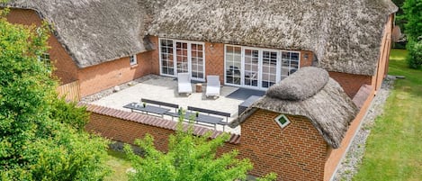 A thatched-roof house with a patio, brick walls, and a large sliding glass door.