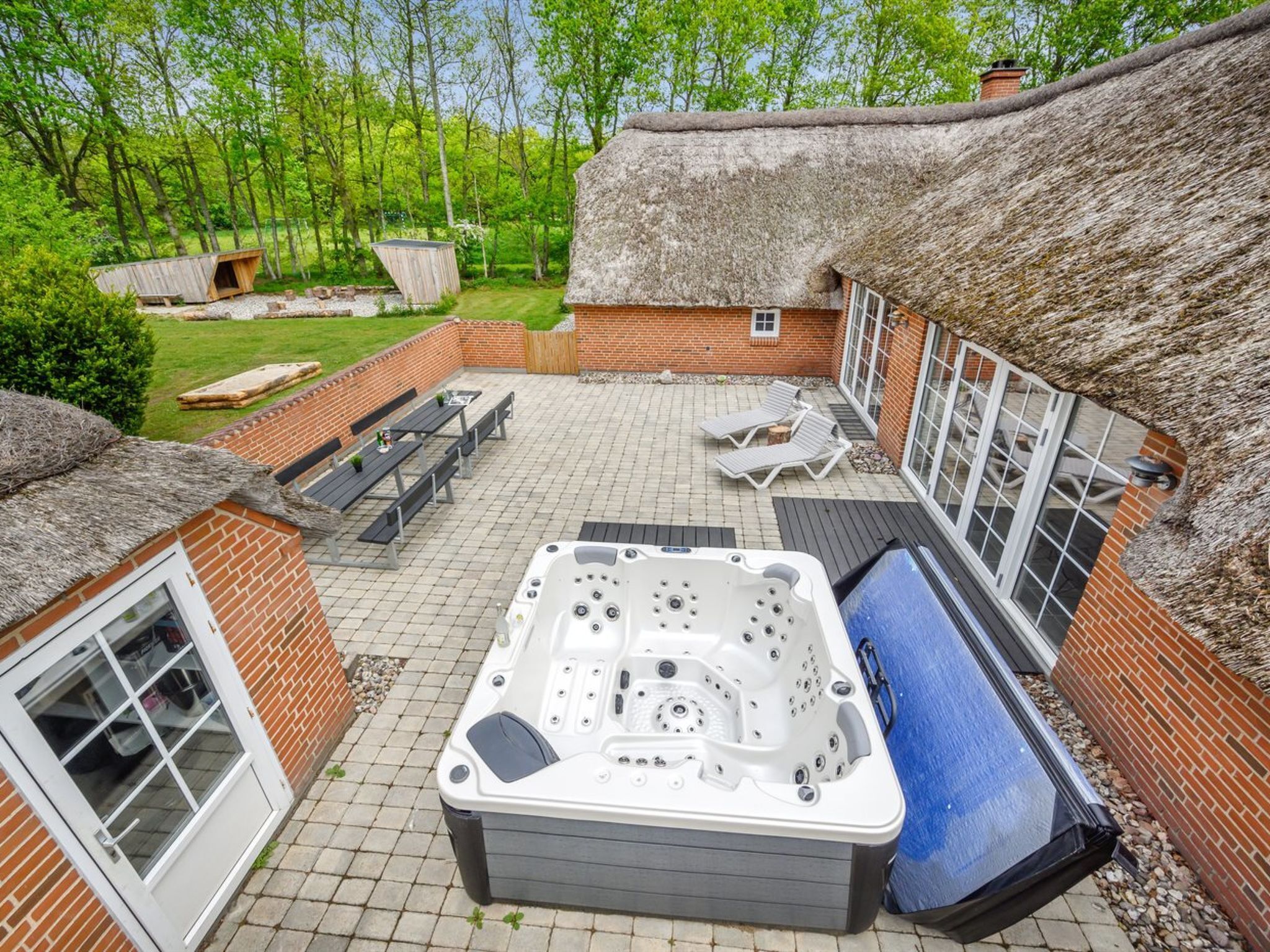 Une terrasse avec un jacuzzi, des sièges d’extérieur et un bâtiment doté d’un toit de chaume.