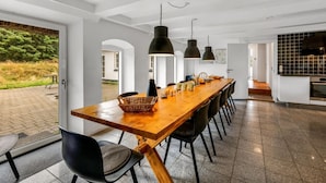 Un comedor moderno con una larga mesa de madera, sillas negras e iluminación colgante.