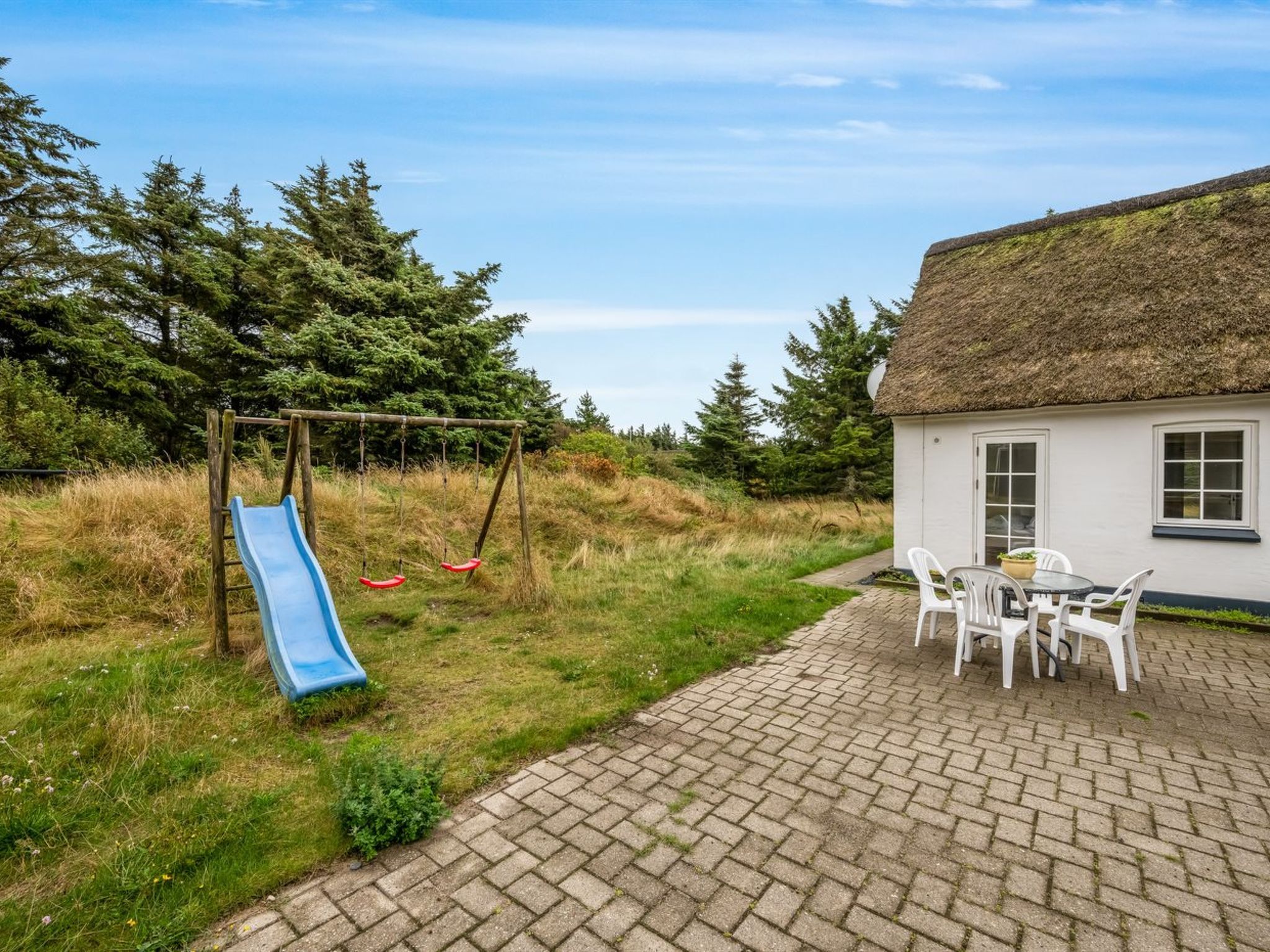 A patio with a brick floor, a white table with chairs, and a thatched-roof building.
