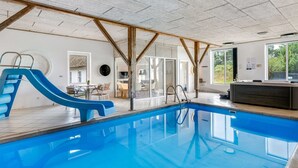 Una piscina interior con tobogán, vigas de madera y vistas al exterior.