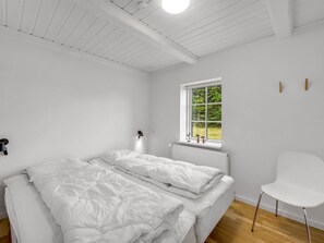 A minimalist bedroom with a large bed, a window with a view of greenery, and a white chair. - "Cornelius" - 900m from the sea by Interhome (Ulfborg)