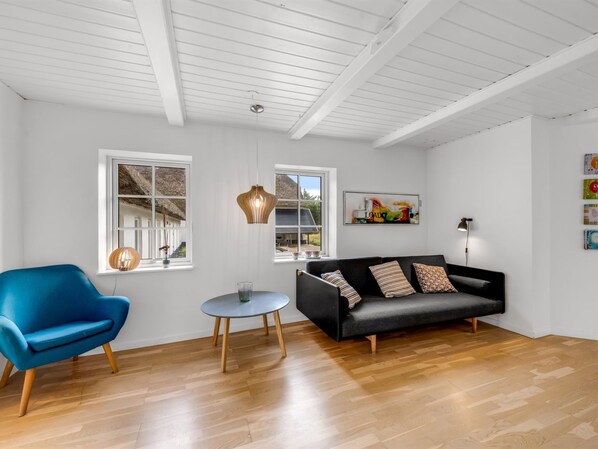 A modern living room with a black sofa, a blue armchair, a small round table, and a pendant light.