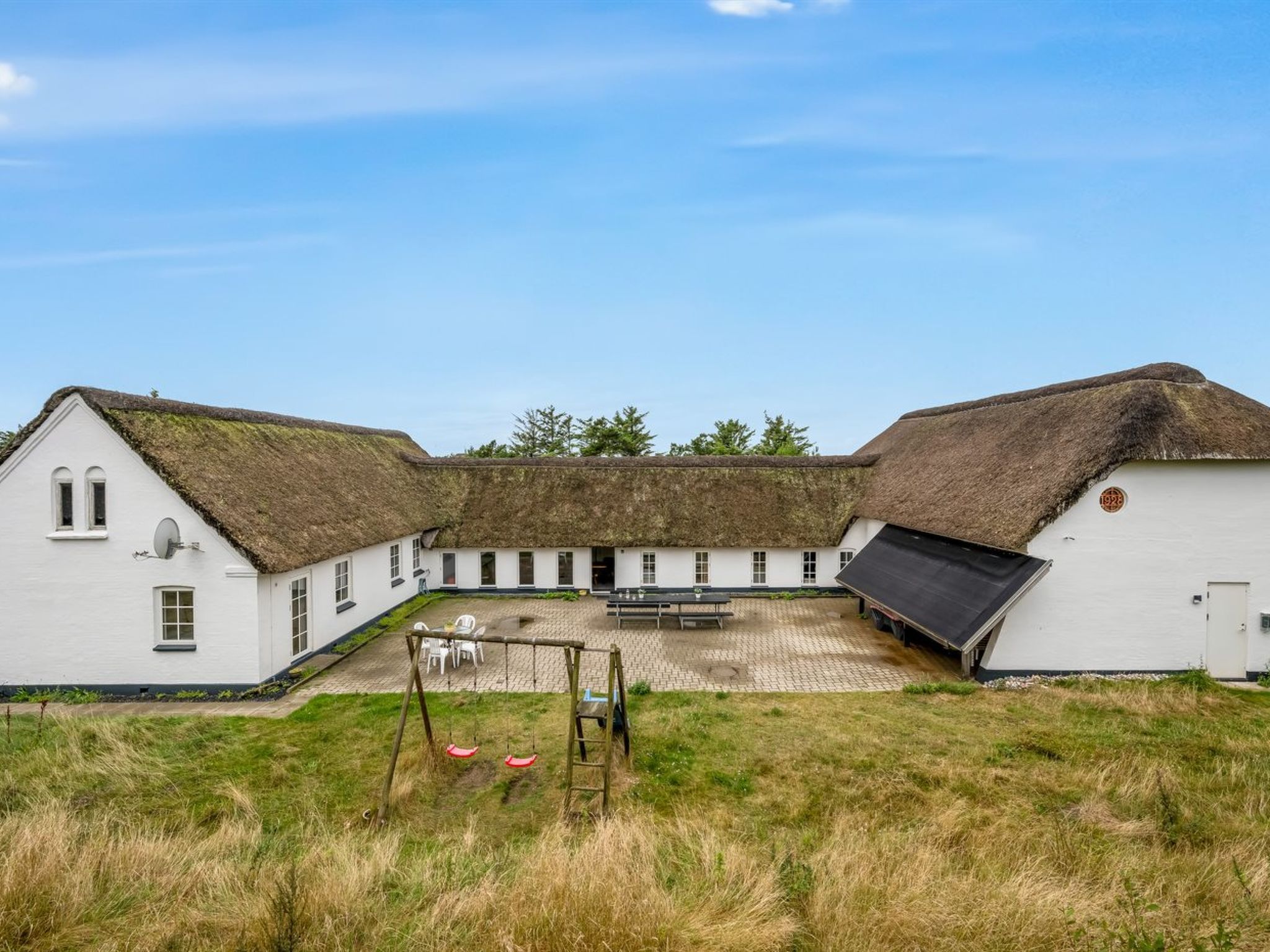 Een traditioneel gebouw met een rieten dak, een binnenplaats met een schommel en een witte gevel.