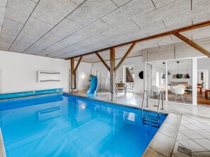 A swimming pool with a clear blue water surface, surrounded by a tiled floor and a ceiling with exposed wooden beams.