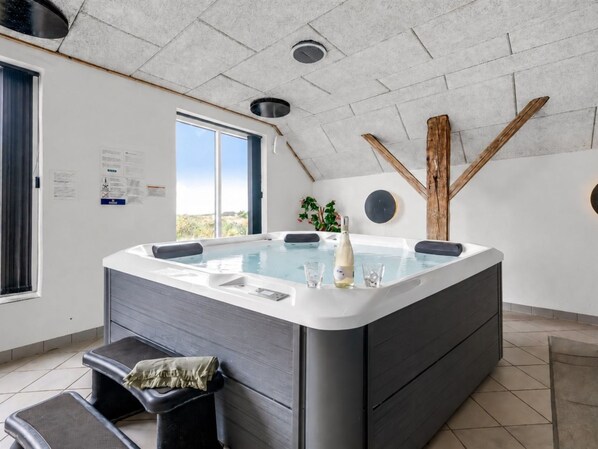 A modern spa room with a hot tub, a window, and a wooden beam structure.