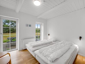 A bedroom with a double bed, a small table, and a view of a park through the window.