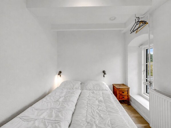 A minimalist bedroom with a single bed, a nightstand, a radiator, and a window. - "Cornelius" - 900m from the sea by Interhome (Ulfborg)