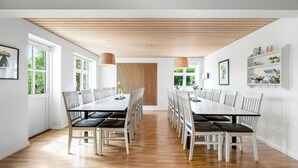 Uma sala de jantar moderna com uma mesa comprida e cadeiras, teto de madeira e janelas grandes.