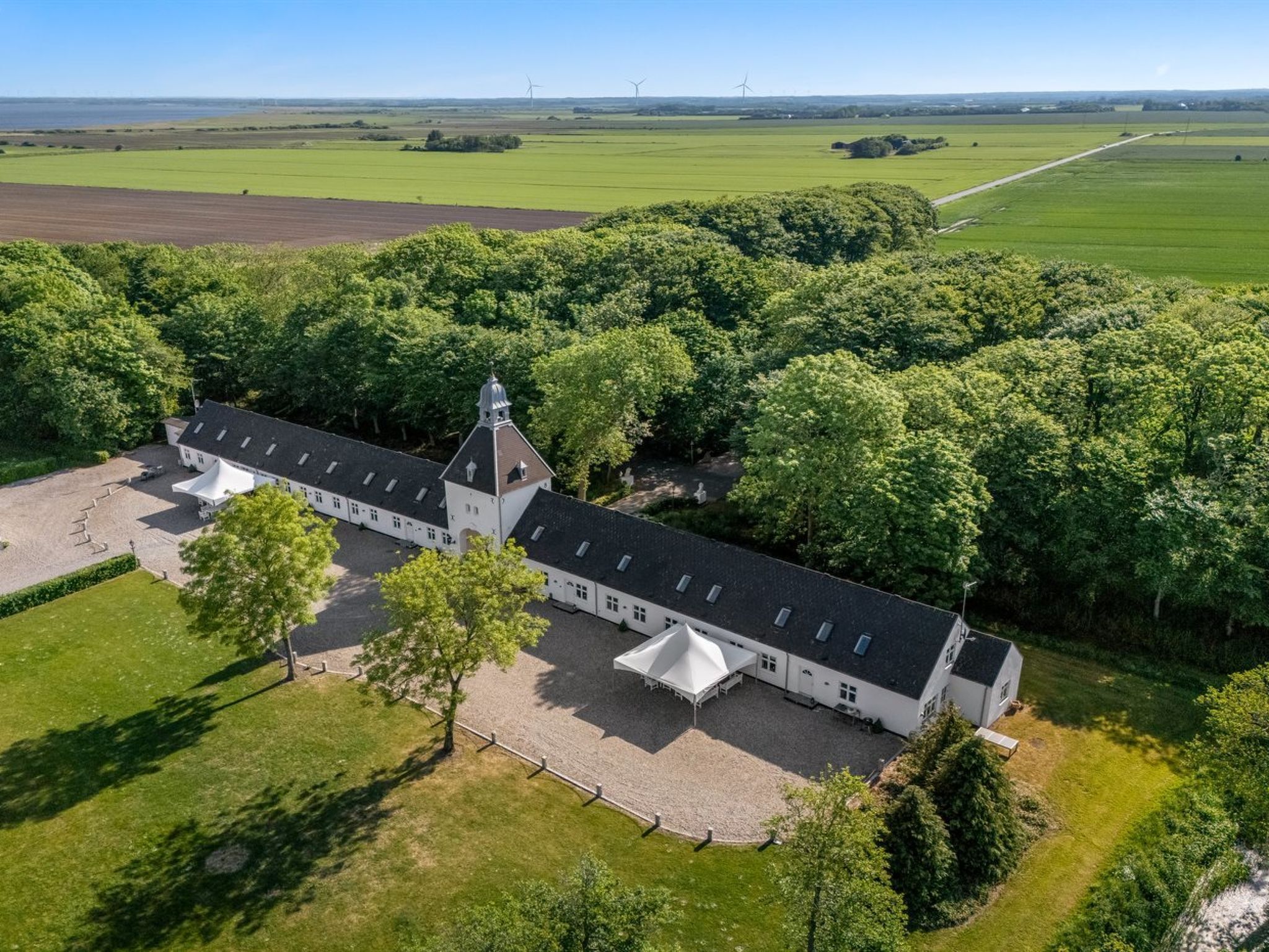 An aerial view of a large, white building with a central tower, surrounded by lush greenery and fields.