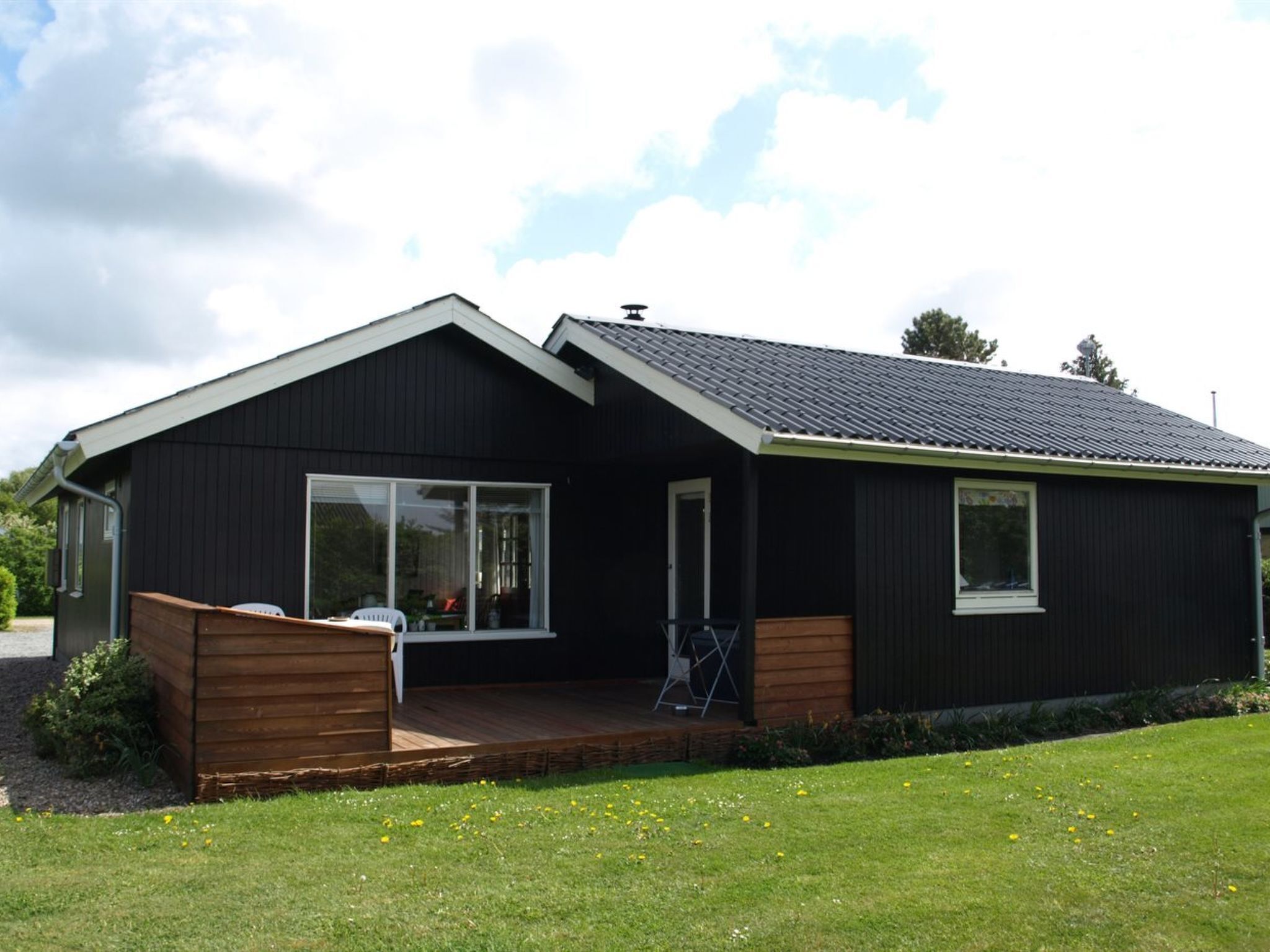 Et moderne etplanshus med mørk facade, skråt tag og en veranda med en træbænk.