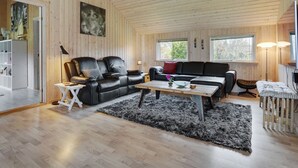 A spacious living room with wooden walls and ceiling, a black leather sofa, a black and white striped ottoman, and a wooden coffee table. - "Hegge" - 300m from the sea by Interhome (Væggerløse)