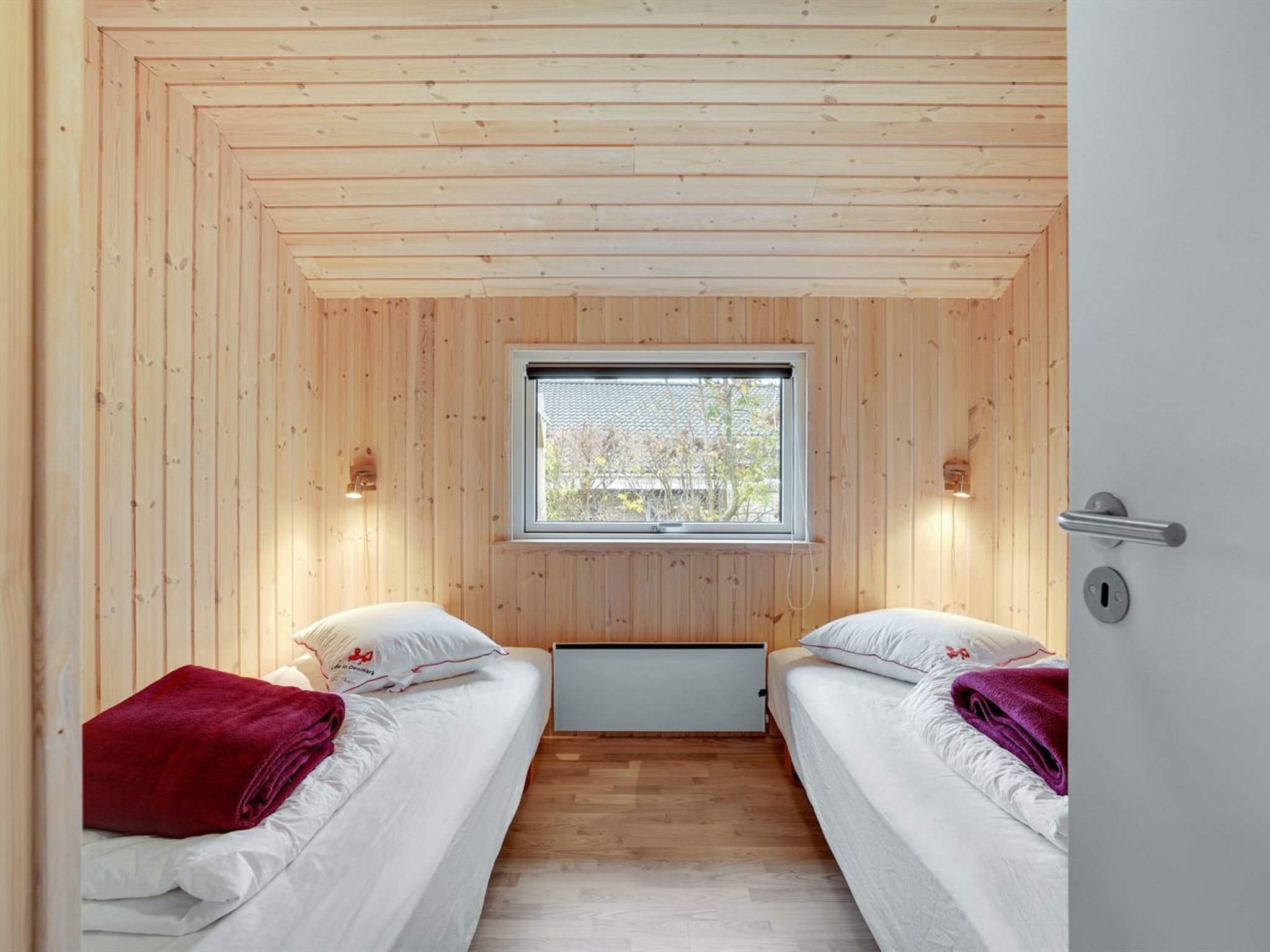 En hytte med to senge, et vindue og en trælofts.