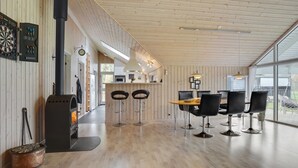 A modern kitchen with wooden paneling, a central island with bar stools, and a large window providing natural light. - "Hegge" - 300m from the sea by Interhome (Væggerløse)