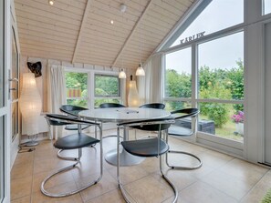Ein moderner Essbereich mit einem runden Tisch und sechs schwarzen Stühlen, großen Fenstern mit Vorhängen und Blick auf Grünflächen.
