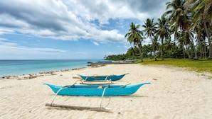 A beach with two blue boats, a sandy shore, and palm trees. - Camotes hidden huts-rooms-bar-restaurant (San Francisco)