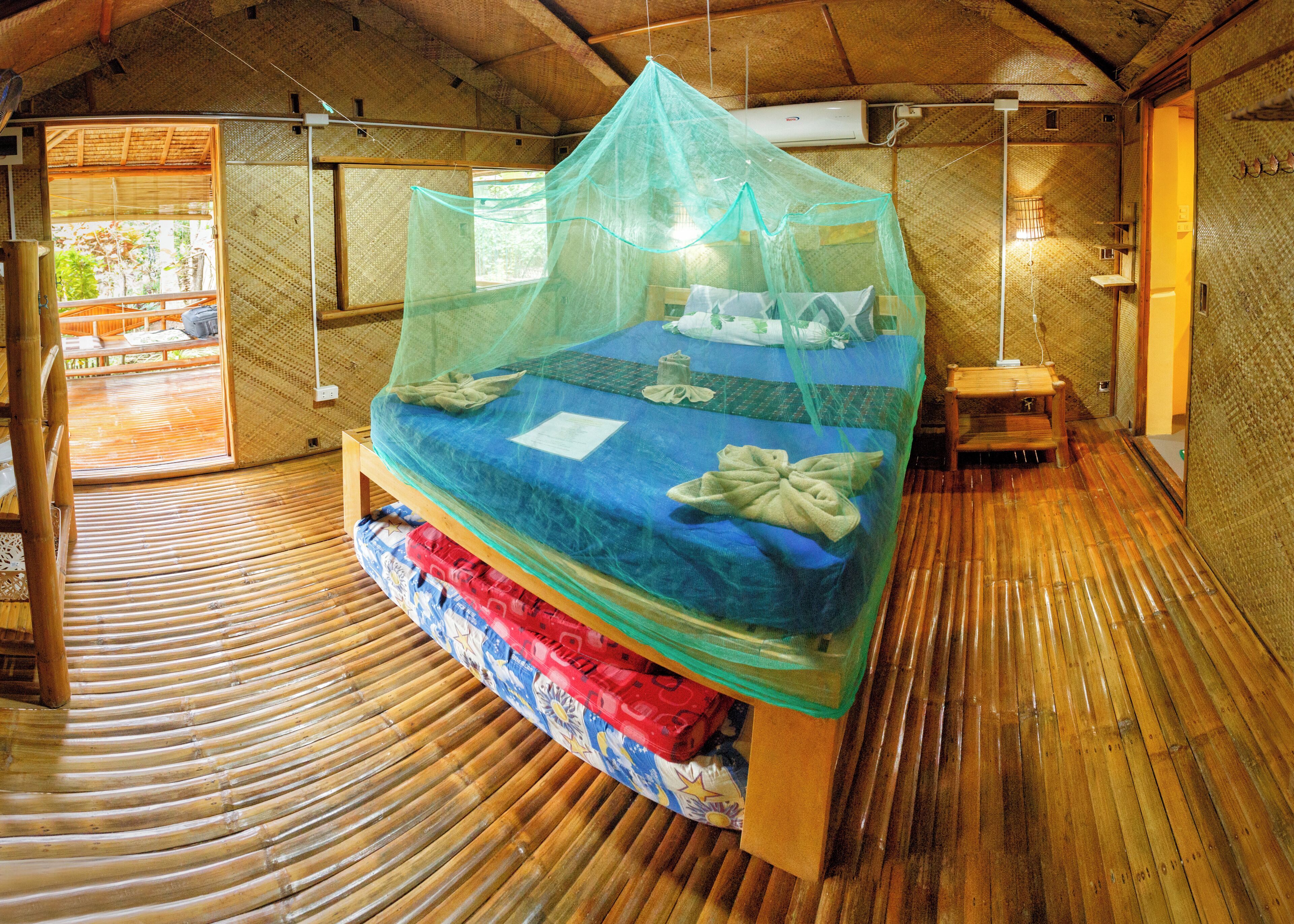 A room with a bed covered by a mosquito net, wooden flooring, and a small table.