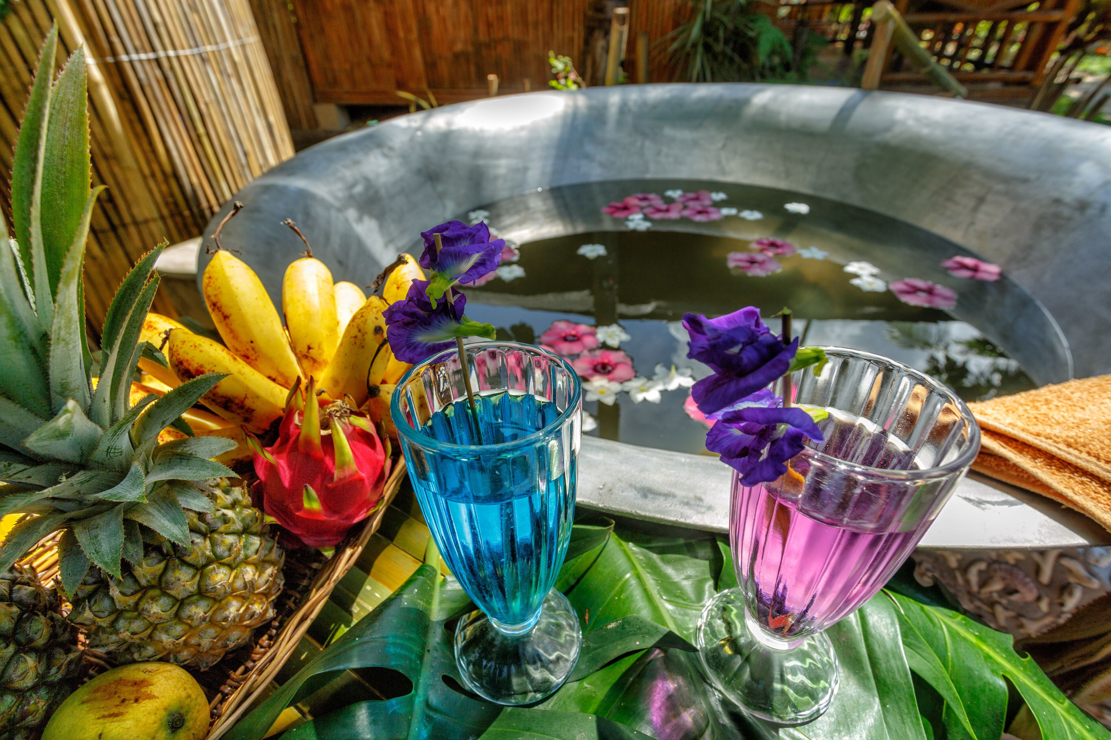 A tropical setting with a fruit basket, two glass cups, and a decorative water feature.