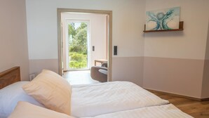Ein Schlafzimmer mit einem Bett, Kissen, einem Holz-Kopfteil, einem Bild an der Wand und Blick ins Freie.