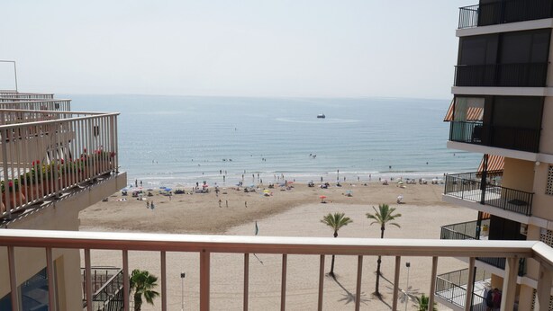 A beach view from a balcony with a clear sky, a sandy beach, and a few people.