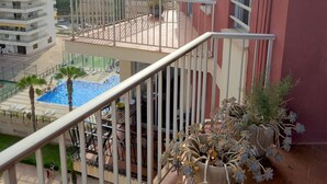 A balcony with a view of a swimming pool, a red building, and a white building with balconies.
