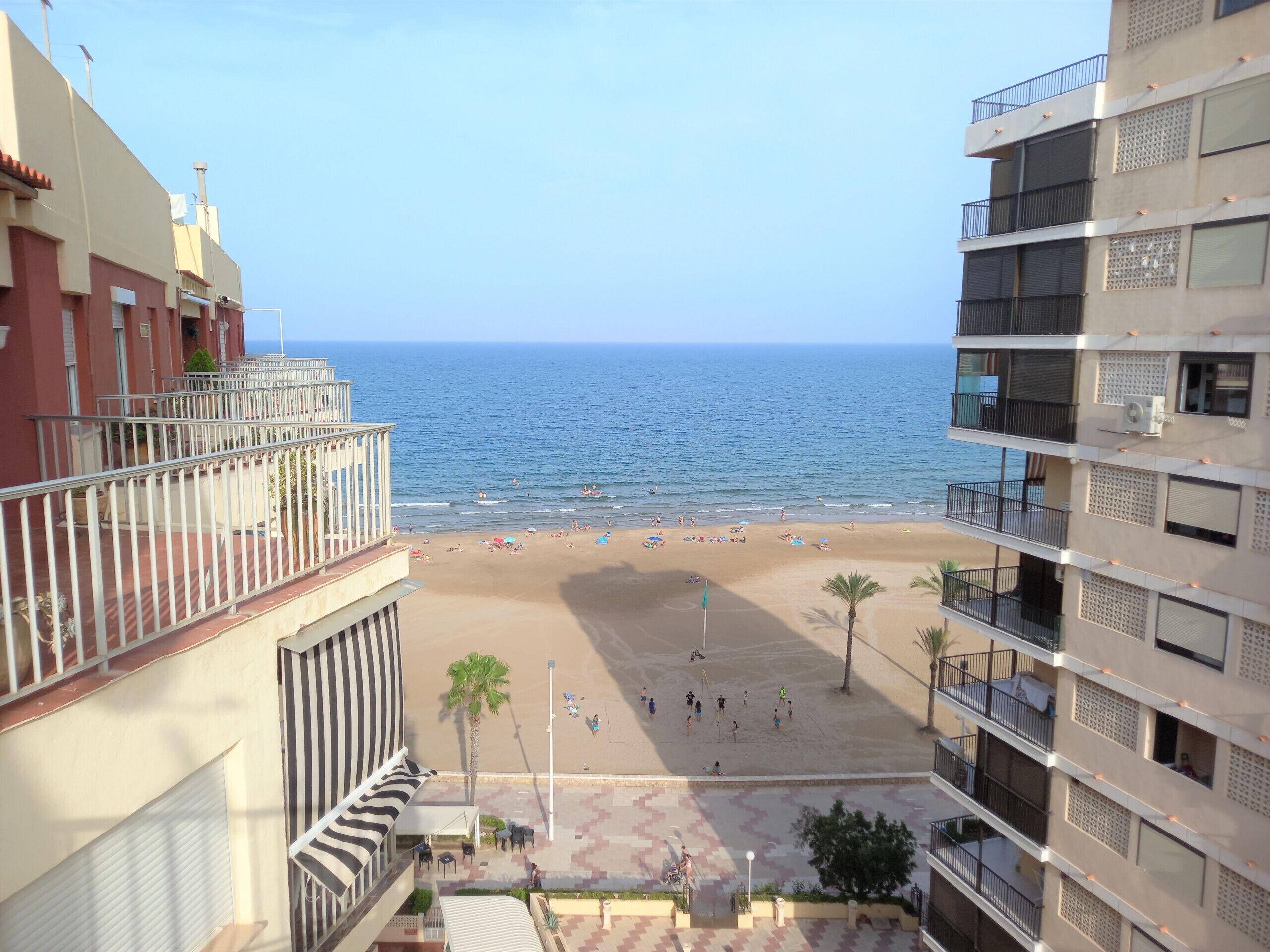 A beach view from a balcony with a clear sky, sandy beach, and ocean.