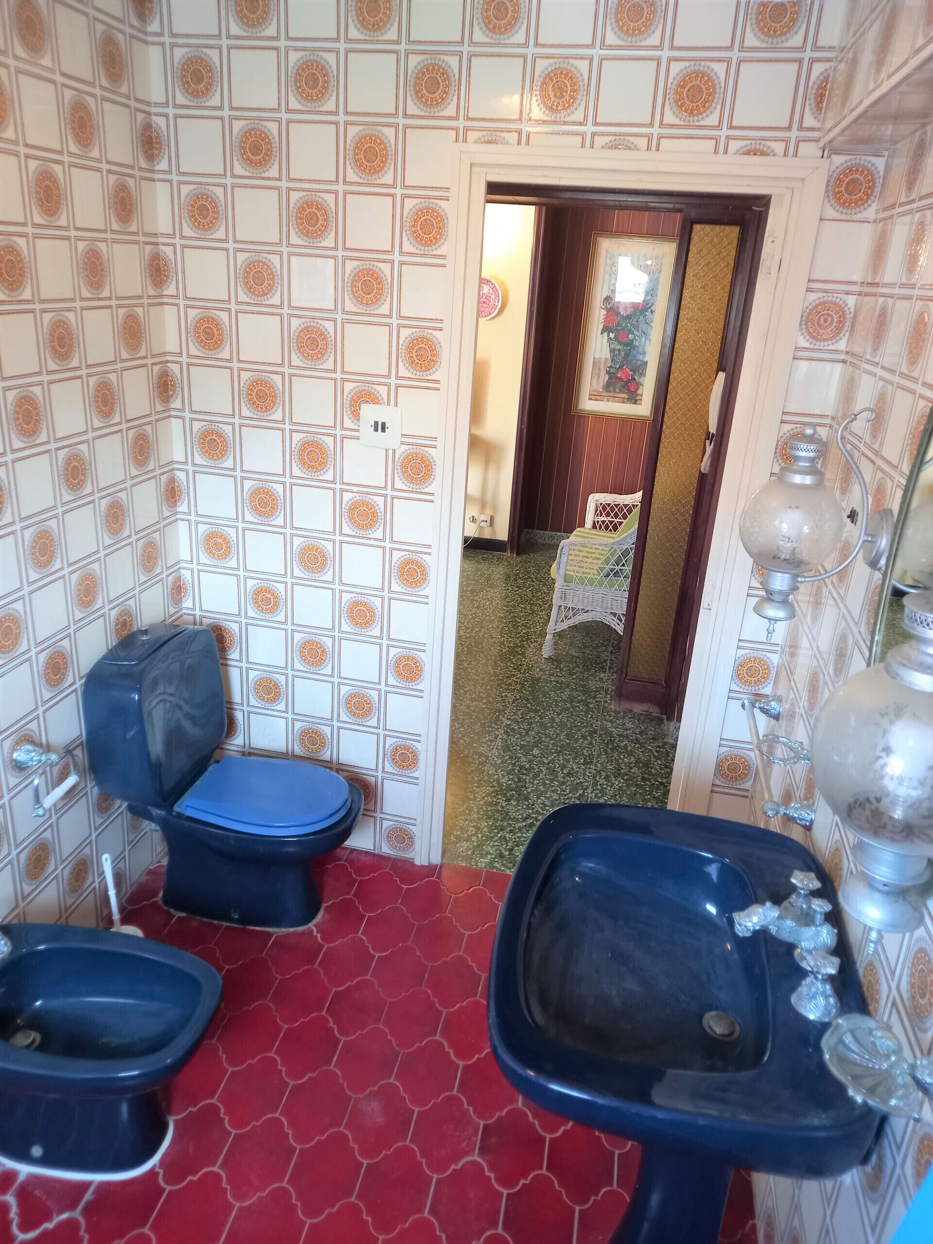 Un bagno con piastrelle decorate, un water, un bidet e un lavandino con un contenitore di vetro ornamentale.