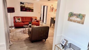 A living room with a red sofa, a brown armchair, a coffee table, and a rug. There is a ceiling fan, a painting on the wall, and a welcome sign. - Elegant 3 Bedrooms with private pool, close to Disney World,Downtown Kissimmee. (Kissimmee)