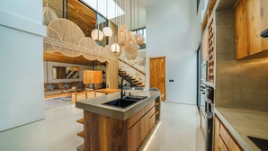A modern kitchen with a central island, wooden cabinetry, and pendant lighting. - Villa Arunika - 2BR Villa (Tabanan)