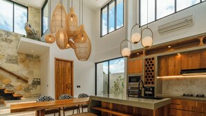 A modern kitchen with a central island, pendant lighting, and large windows. - Villa Arunika - 2BR Villa (Tabanan)