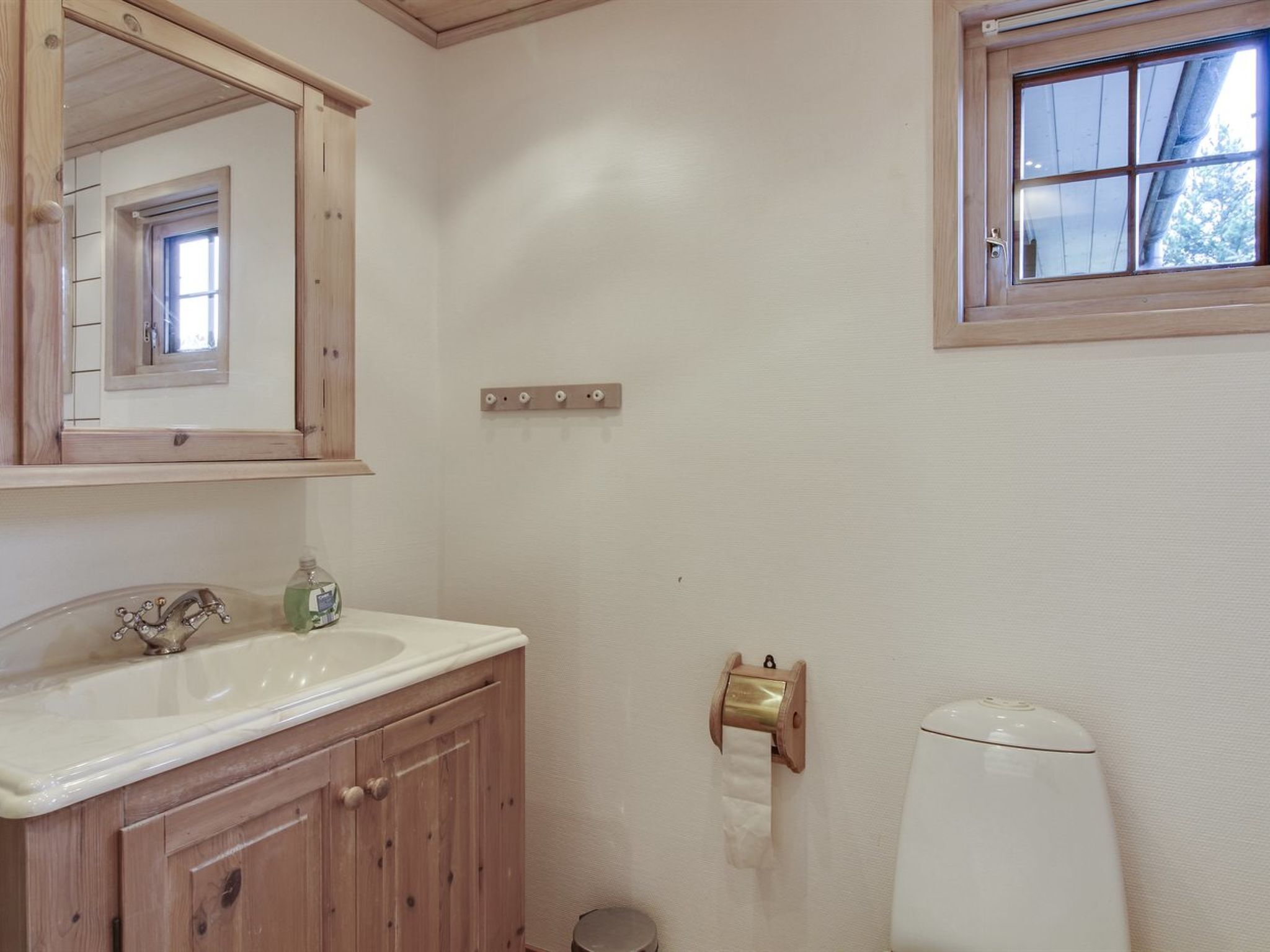 A bathroom with a wooden vanity, a mirror, a toilet, and a window.