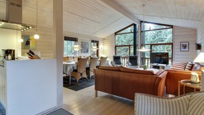 Amplia sala de estar con techo de madera, un sofá, un televisor y un comedor con sillas y una mesa.