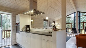 Una cocina moderna con una isla central, armarios blancos y un amplio ventanal con vistas a una terraza.