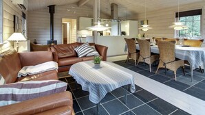 Un comedor acogedor con techo de madera, sofá de cuero marrón y sillas de mimbre alrededor de una mesa con mantel a rayas.