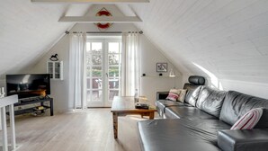 Ein modernes Loft-Apartment mit hohen Decken, einem schwarzen Ledersofa, einem Holztisch, einem Fernseher auf einem Standfuß und einem großen Fenster mit Vorhängen.