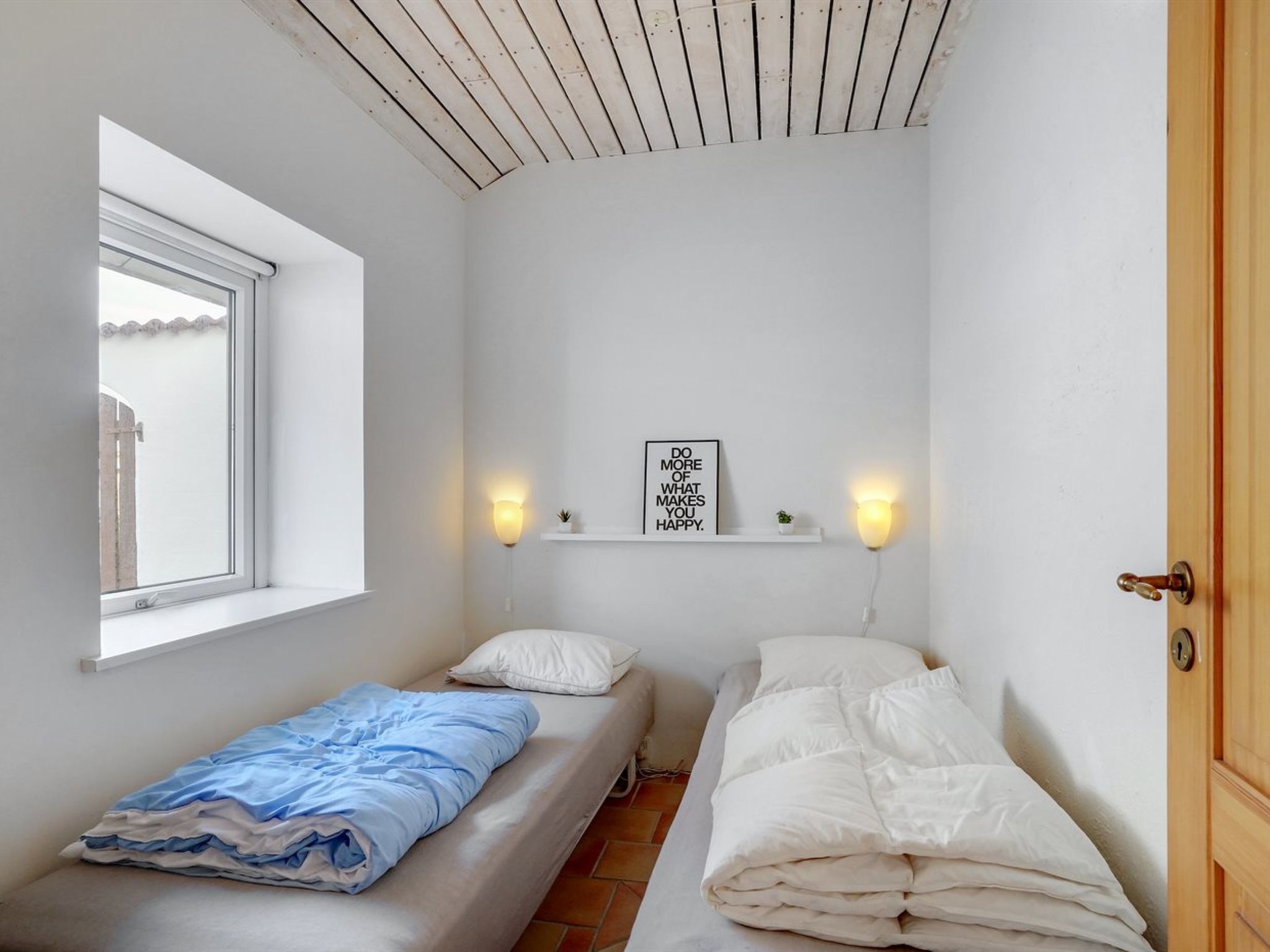 A small, single-room accommodation with two beds, a window, and a motivational wall art piece.