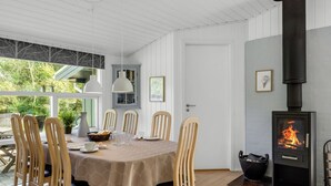 Zona pranzo con tavolo apparecchiato per sei, circondato da sedie di legno, un soffitto bianco e un camino a legna.