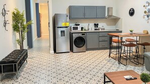 A compact kitchen with a washing machine, a refrigerator, a microwave, and a dining area with stools. - Apartamento en el Corazón de Casco Viejo Panamá 14 (Panamá)