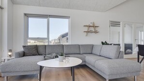 Un salon moderne avec un canapé d’angle gris, une table basse ronde blanche et une étagère en bois agrémentée d’objets décoratifs.