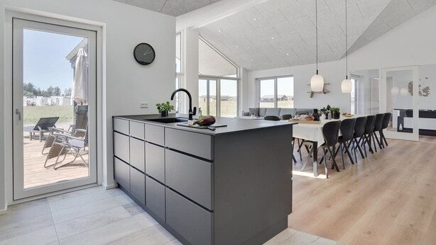 Une cuisine moderne dot ée d’un grand îlot central, d’un coin repas avec une longue table et des chaises, et offrant une vue sur l’extérieur.