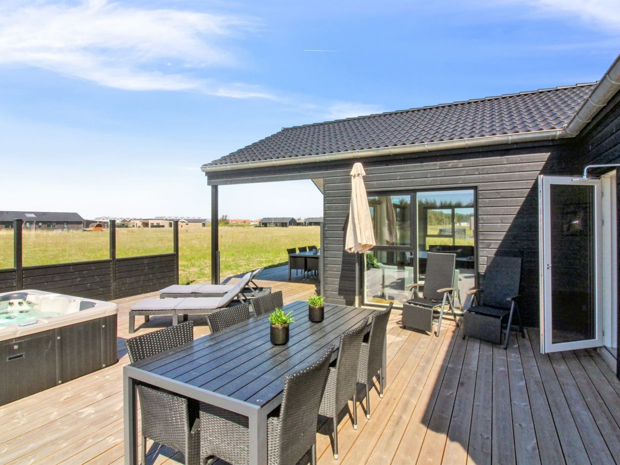 Eine Terrasse mit Gartenmöbeln, einem Whirlpool und einer überdachten Sitzgelegenheit mit Blick auf die umliegende Landschaft.