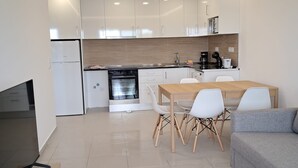 A modern kitchen with white cabinets, a built-in oven, and a dining area with a wooden table and white chairs. - T1 TENIS GOLFMAR - PISCINA- WIFI- VILAMOURA (Vilamoura)
