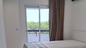 A hotel room with two beds, a large window with curtains, and an air conditioning unit. - T1 TENIS GOLFMAR - PISCINA- WIFI- VILAMOURA (Vilamoura)