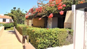 A residential building with a tiled roof, a covered porch, and a well-maintained garden with flowering plants and hedges.