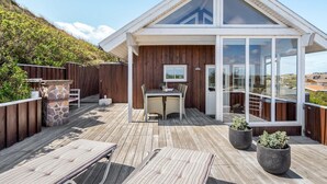 A modern house with a wooden deck, a dining area, and a large glass door leading to a balcony.