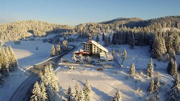 Un albergue cubierto de nieve con un telesilla, rodeado de bosques densos y árboles nevados.